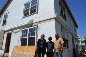 three people stand in front of home under construction